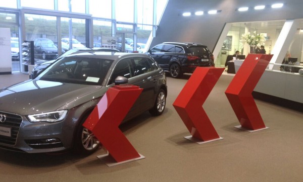 Bespoke red acrylic 3d arrows that are displayed beside showroom cars in an Audi garage