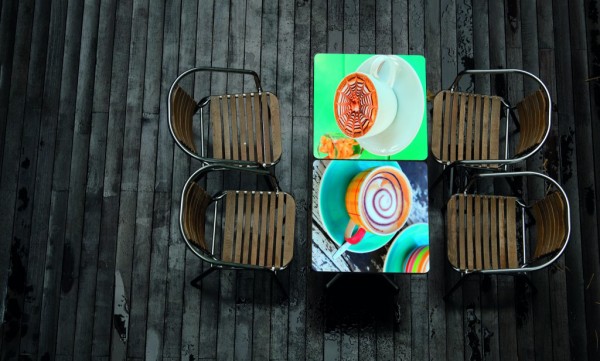 Two Chromaluxe tabletops with colourful coffee cups printed, displayed on a grey decking